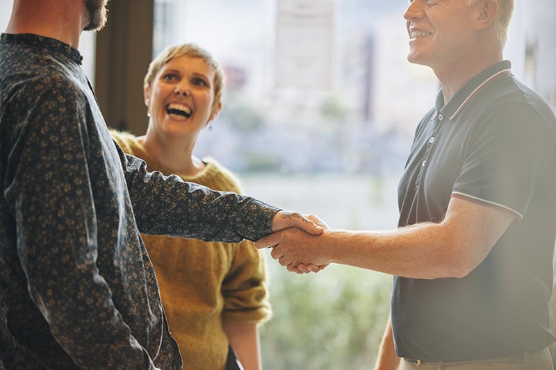 Kollegaer står smilende sammen og giver hinanden i hånden efter godt teamwork.