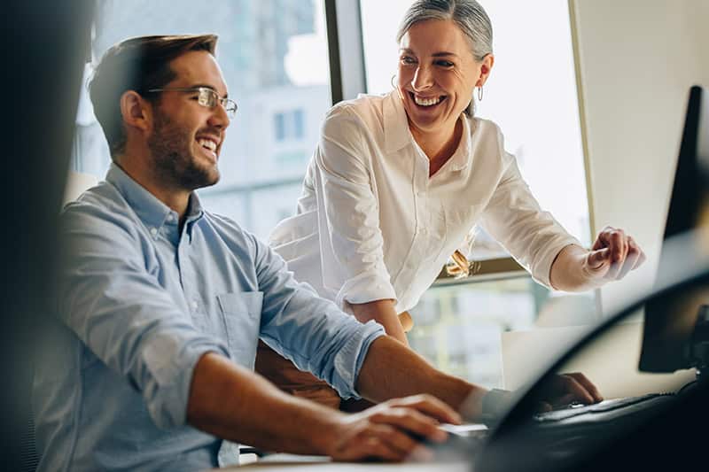 Kvindelig leder står ved medarbejders skrivebord i et godt teamarbejde på arbejdspladsen.